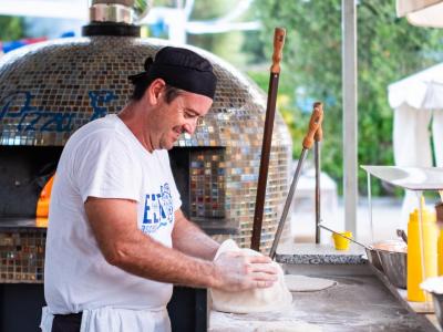 Pizzaiolo prepara l'impasto vicino a un forno a legna.