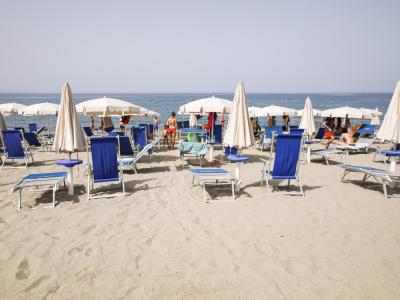 Spiaggia con lettini blu e ombrelloni bianchi, vista mare.