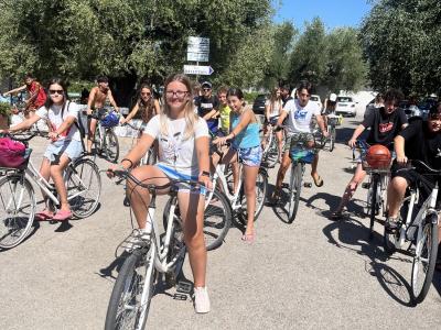 Gruppo di giovani in bici sotto il sole, tra alberi verdi.