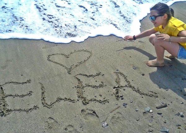 Bambina scrive 'Ewa' sulla sabbia con un cuore.