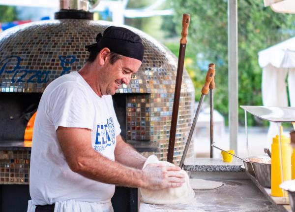 Pizzaiolo prepara l'impasto vicino a un forno a legna.