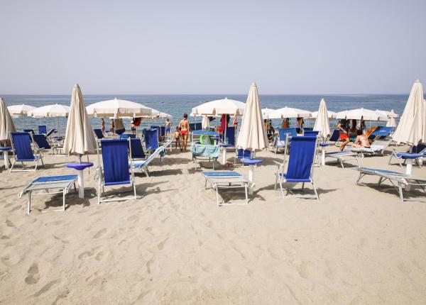 Spiaggia con lettini blu e ombrelloni bianchi, vista mare.