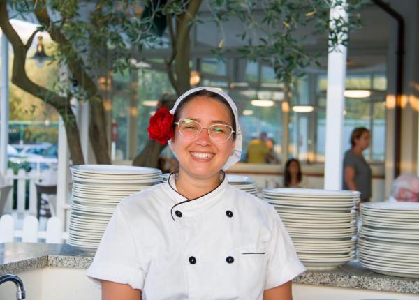 Chef sorridente con fiore rosso nei capelli, davanti a piatti impilati.
