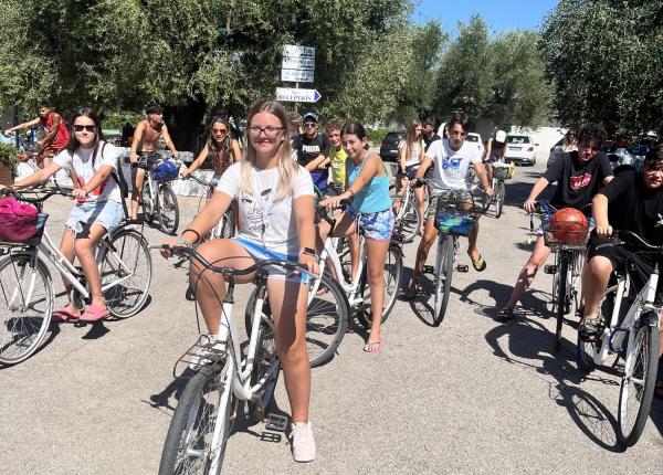 Gruppo di giovani in bici sotto il sole, tra alberi verdi.