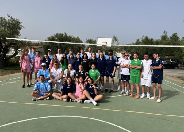 Gruppo di giovani sorridenti in divise colorate su un campo da pallavolo all'aperto.